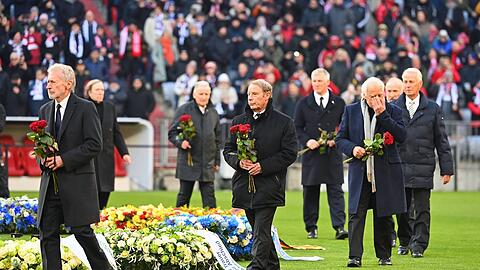 Elf Wegbegleiter Beckenbauers legen um den Mittelkreis Rosen nieder.
