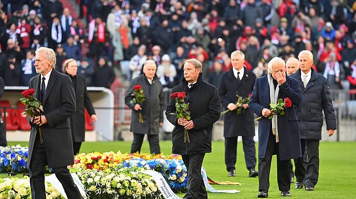 Elf Wegbegleiter Beckenbauers legen um den Mittelkreis Rosen nieder.