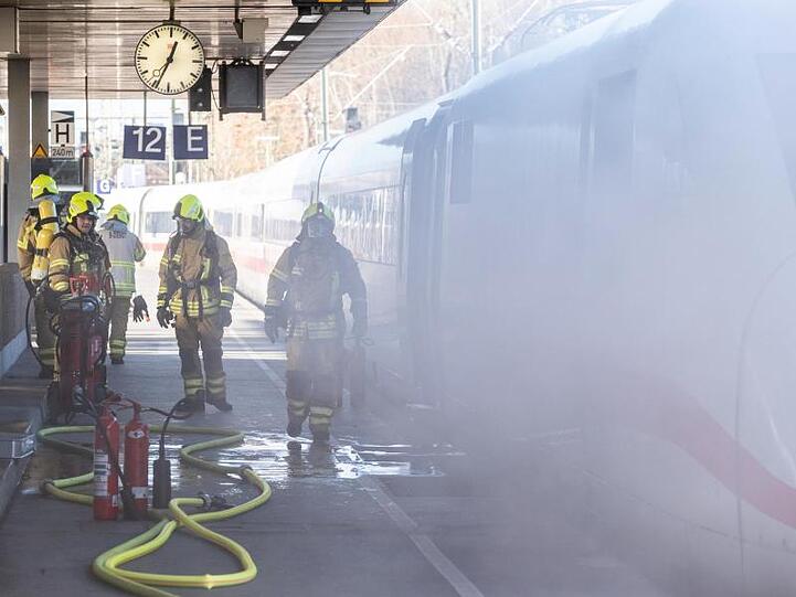 Feuerwehrleute stehen an dem in Brand geratenen ICE.