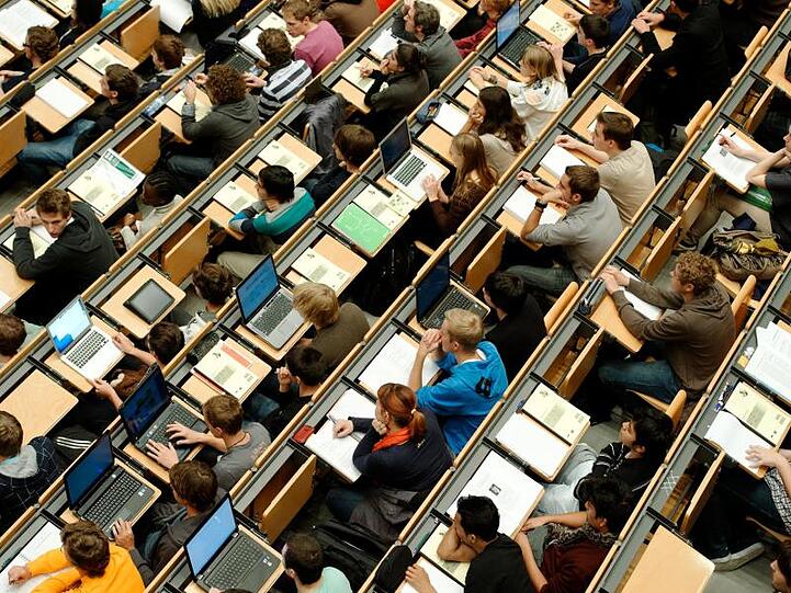 Studenten sitzen in einem großen Hörsaal der Technischen Universität (TUM). Foto: Peter Kneffel/Archiv