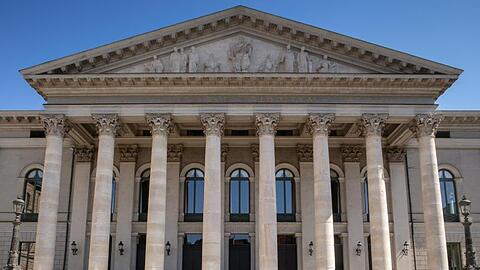 Passanten sitzen auf der Treppe vor der bayerischen Staatsoper.