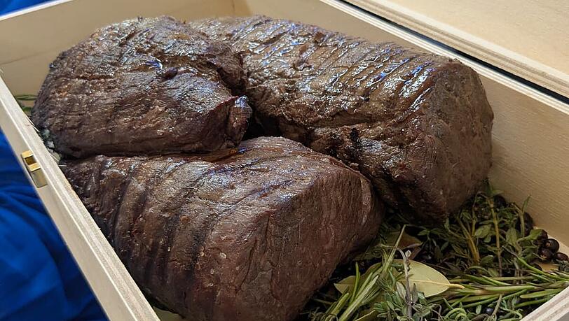 Das ger&auml;ucherte Filet vom Steirischen Almochsen wird in einer Holzbox am Tisch pr&auml;sentiert.