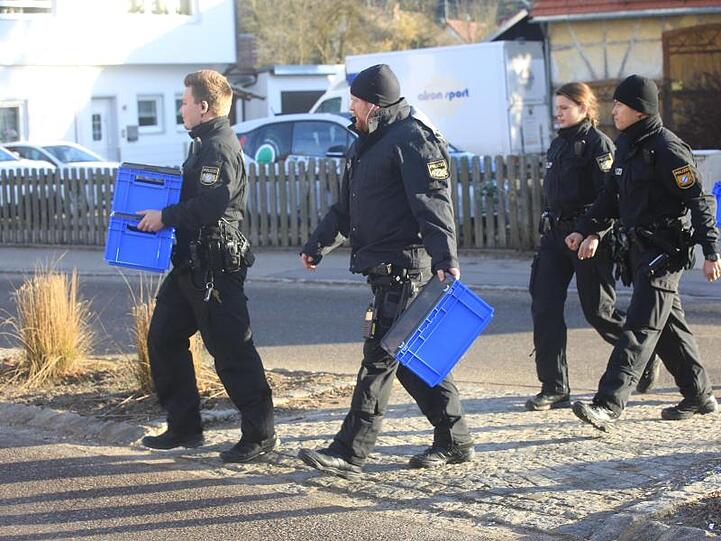 Polizeibeamte überqueren mit blauen Kisten in den Händen eine Straße. Foto: Ralf Zwiebler/dpa