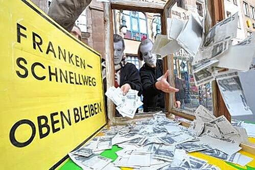 Verkleidet mit Maly- und Söder-Masken (li.) protestieren die Grünen gegen die Geldverschwendung am Frankenschnellweg.