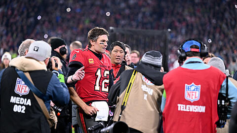 Tom Brady (M), Quarterback der Tampa Bay Buccaneers, läuft nach dem Spiel an Medienvertretern vorbei über den Rasen.