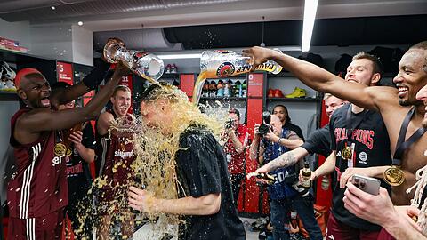 Der FC Bayern Basketball ist Pokalsieger 2024: Die Münchener Isaac Bonga (l) und Serge Ibaka (r) geben Andreas Obst (M) eine Bierdusche.