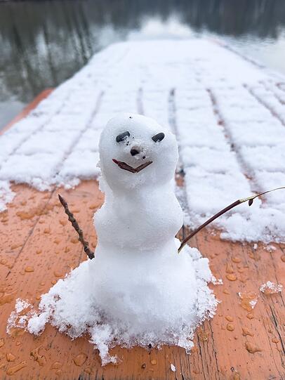 Ein kleiner Schneemann steht auf einem schneebedeckten Biertisch in einem Biergarten im Englischen Garten.