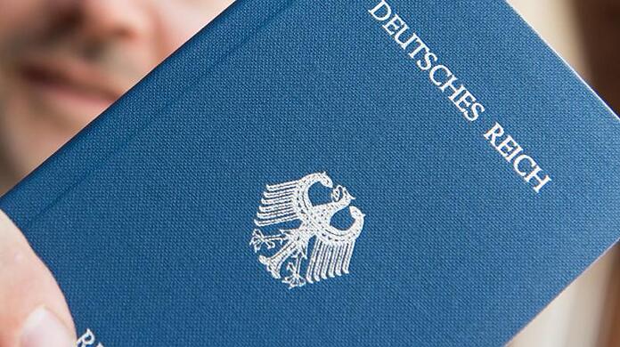 Ein Mann hält ein Heft mit dem Aufdruck "Deutsches Reich Reisepass" in der Hand.