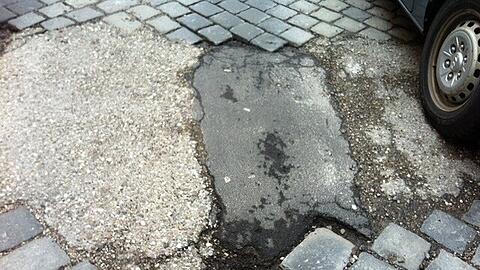 Löcher in der Teerdecke, gleich daneben parkt ein Auto.