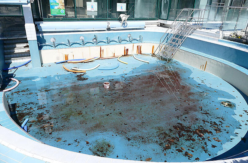 Regenwasser und Laub liegen neben Schwimmrollen im Außenbecken.