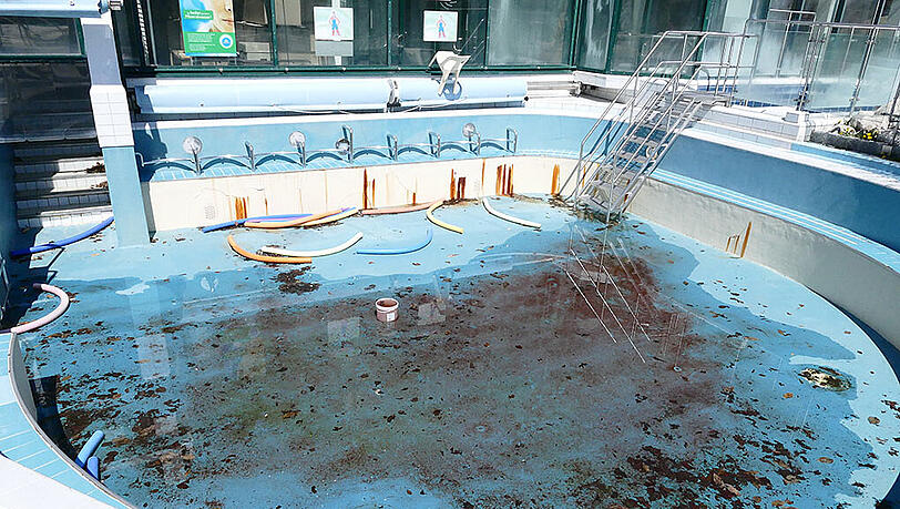 Regenwasser und Laub liegen neben Schwimmrollen im Außenbecken.