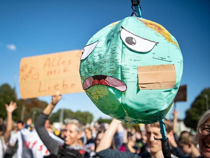 Demonstranten halten einen Luftballon mit Globusaufdruck hoch, der unglücklichen Gesichtszügen beklebt ist. Foto: Sina Schuldt/Archivbild