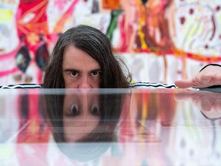Jonathan Meese, Maler und Aktionskünstler, spiegelt sich in dem noch geschlossenen Ausstellungsraum in einem Schaukasten. Foto: Lino Mirgeler