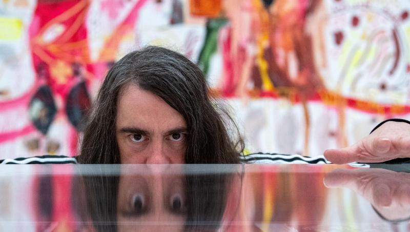 Jonathan Meese, Maler und Aktionskünstler, spiegelt sich in dem noch geschlossenen Ausstellungsraum in einem Schaukasten. Foto: Lino Mirgeler