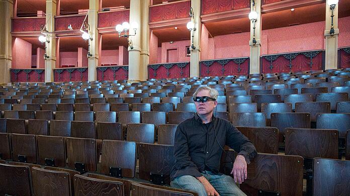 Jay Scheib sitzt mit einer Augmented Reality Brille im Zuschauerraum des Festspielhauses.