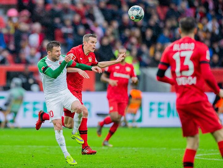 Leverkusens Sven Bender (r) und Augsburgs Daniel Baier versuchen an den Ball zu kommen. Foto: Rolf Vennenbernd/dpa