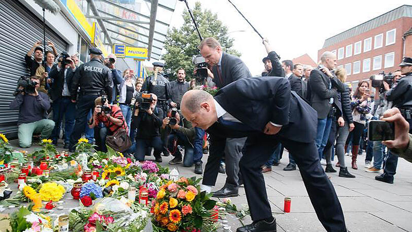 Hamburgs Erster Bürgermeister Olaf Scholz (vorne) und Innensenator Andy Grote legen in Hamburg-Barmbek vor dem Supermarkt ab, in dem die tödliche Attacke stattfand.