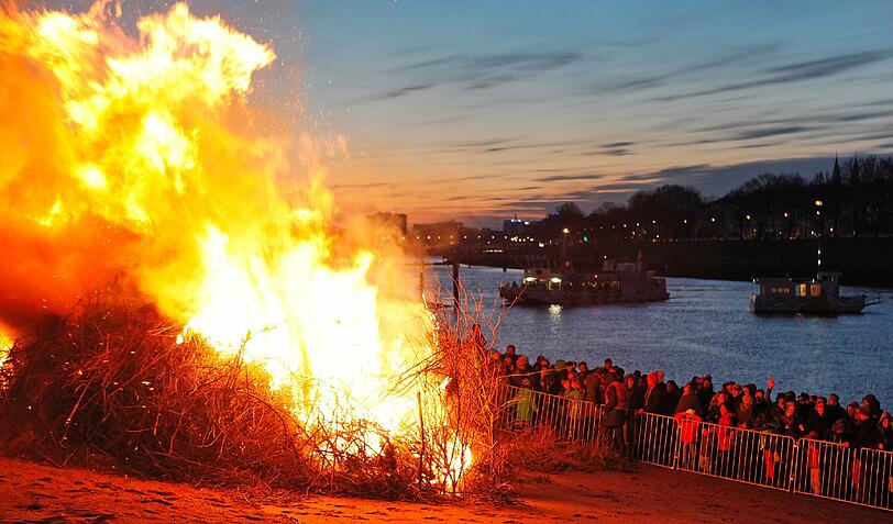 Zuschauer beobachten am Samstag (07.04.12) das Osterfeuer am Weserstrand in Bremen, waehrend im Hintergrund die Faehrschiffe "Das Schiff" (l.) und "Hal Oever" auf der Weser pendeln. Allein in der Hansestadt sind fuer das Osterwochenende rund 90 oeffentliche und private Feuer angemeldet worden, mit denen, einer vorchristlichen Tradition folgend, der Winter ausgetrieben werden soll.