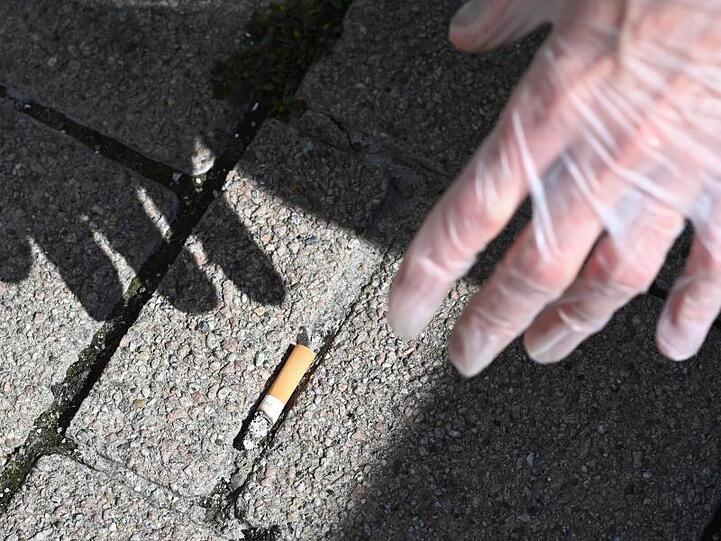 Ein Mann sammelt eine Zigarettenstummel vom Boden auf.