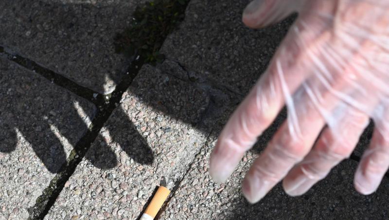 Ein Mann sammelt eine Zigarettenstummel vom Boden auf. Ein Mann sammelt eine Zigarettenstummel vom Boden auf.