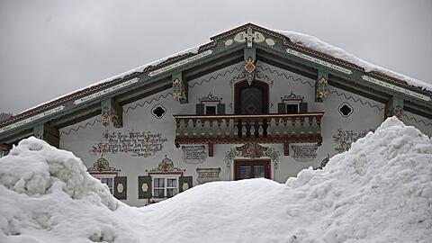 Schneeberge türmen sich vor einem mit Sinnsprüchen und Lüftlmalerei verzierten Haus in Inzell auf.