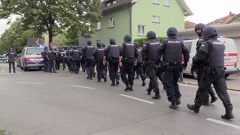 Polizisten mit Helmen und schusssicheren Westen gehen über eine Straße in der Nähe des Tatorts.