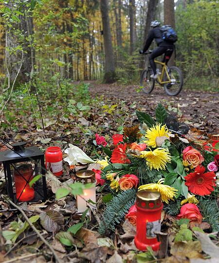 Ein Radfahrer fährt am Montag (31.10.2011) im Siebentischwald in Augsburg (Schwaben) an Blumen und Kerzen vorbei. In der Nacht zum Freitag (28.10.2011) war an dieser Stelle bei einer Schießerei ein Polizist getötet und eine weitere Beamtin verletzt worden. Die Täter flohen in ein großes Waldgebiet und wurden bisher nicht gefasst.
