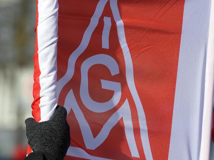Eine mit einem Handschuh bekleidete Hand rollt vor einem Tagungshotel eine Fahne der IG Metall aus. Foto: Stefan Puchner/Archiv