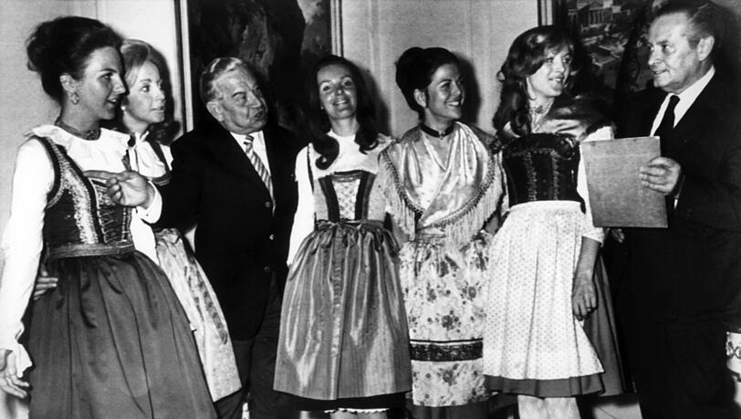 Silvia Sommerlath (3.v.r.) zeigt mit anderen Hostessen dem bayerischen Ministerpr&auml;sidenten Alfons Goppel (l.) und dem deutschen NOK-Pr&auml;sident Willi Daume in M&uuml;nchen die Hostessen-Trachten.