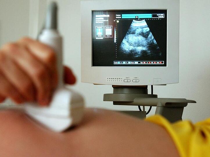Eine Hebamme untersucht mit Ultraschall den Bauch einer Schwangeren