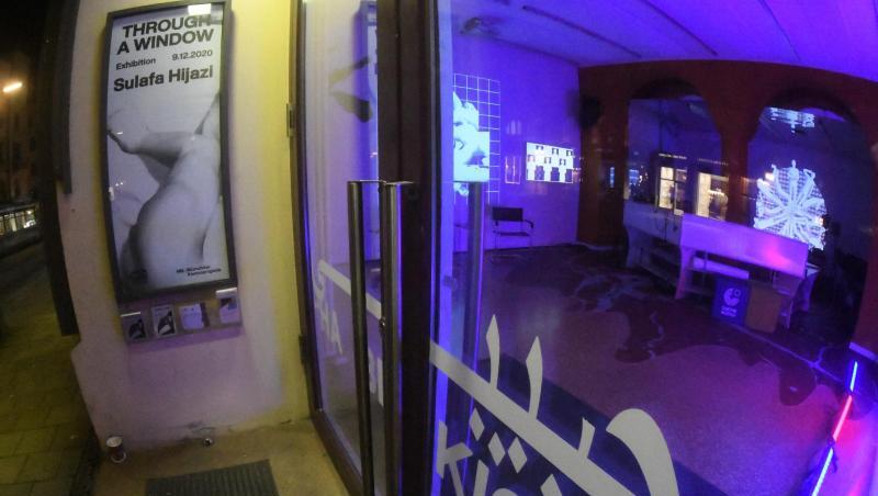 In blauem Licht leuchtet der Innenraum des Habibi Kiosk der Münchner Kammerspiele in der Maximilianstrasse, auf der eine Trambahn fährt.