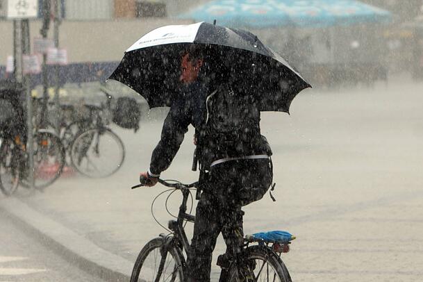 Ein Mann mit Regenschirm radelt &uuml;ber den Marienplatz w&auml;hrend eines Wolkenbruchs mit Gewitter.