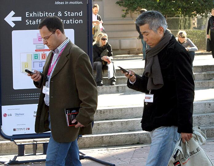 Zwei Besucher beim Mobile World Congress schauen auf ihr Smartphone.(Symboldbild).