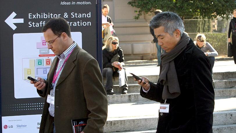 Zwei Besucher beim Mobile World Congress schauen auf ihr Smartphone.(Symboldbild). Zwei Besucher beim Mobile World Congress schauen auf ihr Smartphone.(Symboldbild).