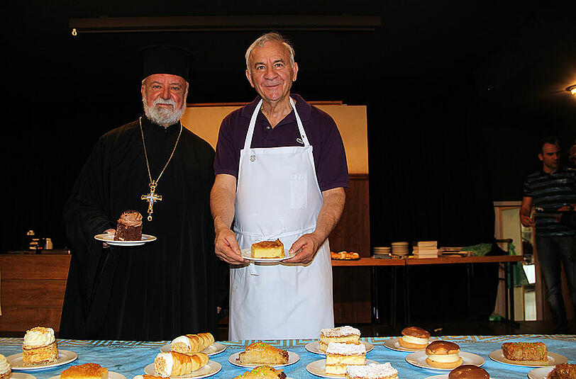 Stylianos Klastos (r.) mit seinem Lieblingsgebäck &bdquo;Galaktompoureko&ldquo; und daneben der Erzpriester Apostolos Malamoussis.