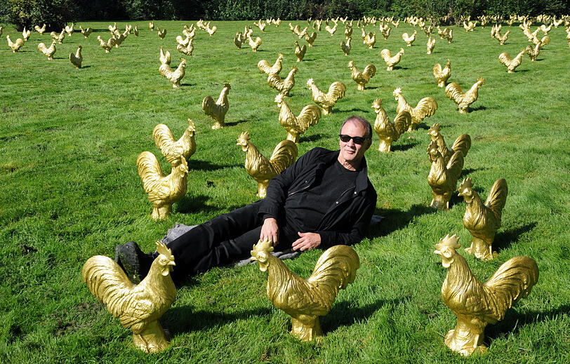 Der K&uuml;nstler Ottmar H&ouml;rl 2011 auf einer Wiese in einer Parkanlage in Haan bei D&uuml;sseldorf zwischen goldenen Plastik-H&auml;hnen,Als Vorlage f&uuml;r das Projekt diente dem K&uuml;nstler der auf dem Stadtwappen abgebildete Hahn. Er gilt als Sinnbild des kampfesfrohen Geistes der B&uuml;rger f&uuml;r die Interessen ihrer Heimat.