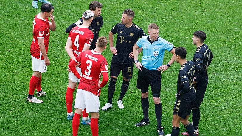 Schiedsrichter Christian Dingert steht gemeinsam mit Spielern während einer Spielpause auf dem Feld. Schiedsrichter Christian Dingert steht gemeinsam mit Spielern während einer Spielpause auf dem Feld.