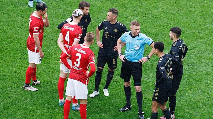 Schiedsrichter Christian Dingert steht gemeinsam mit Spielern während einer Spielpause auf dem Feld.