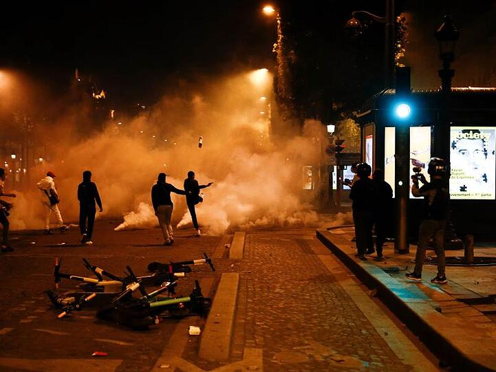 Fans von Paris Saint-Germain treten auf der Champs-Elysées gegen Tränengaskanister.