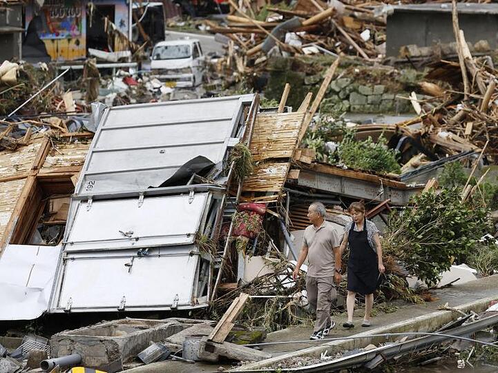 Ein Paar geht durch ein Trümmerfeld. Die Zahl der Todesopfer in den von schweren Unwettern heimgesuchten Überschwemmungsgebieten im Südwesten Japans ist weiter gestiegen.