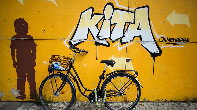Ein Fahrrad lehnt an einer Wand mit einem Graffiti "KiTa". (Symbolbild)