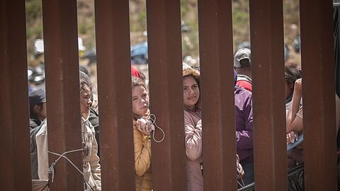 Menschen stehen hinter der Grenzmauer zwischen Mexiko und USA und hoffen darauf, in die USA einreisen zu können.