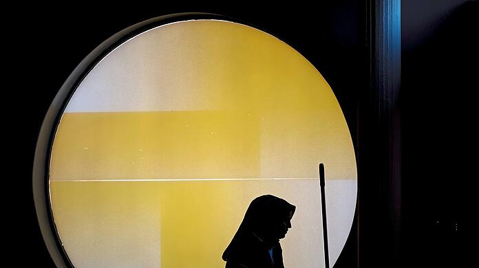 Eine Frau mit einem Wagen für Reinigungsmaterial steht vor einem runden Fenster der Berliner Philharmonie. Um Lohndumping entgegenzuwirken, hat der Gesetzgeber in zahlreichen Bereichen, darunter das Gebäudereinigungsgewerbe, branchenspezifische Mindestlöhne eingeführt.