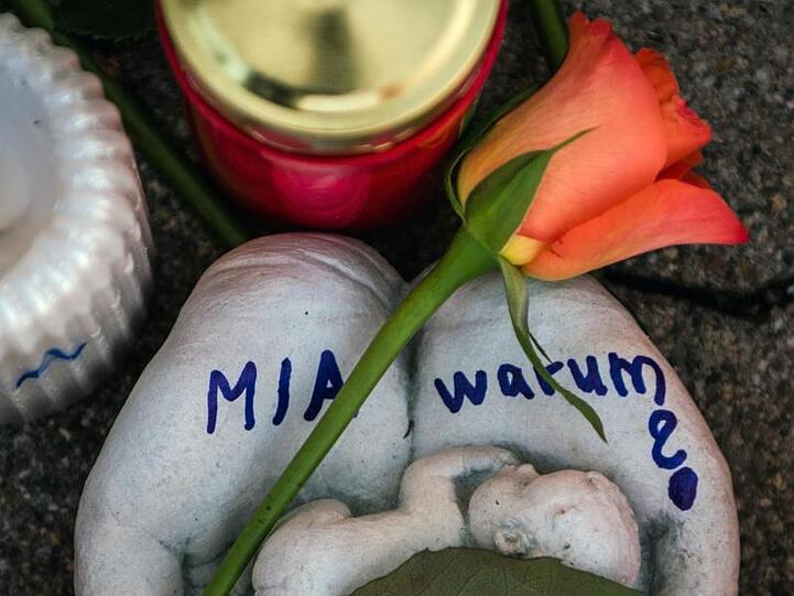 Eine Skulptur in Form zweier Handflächen mit der Aufschrift "Mia warum?" und eine Rose liegen vor dem Drogeriemarkt, in die 15-jährige Mädchen von ihrem Ex-Freund erstochen wurde.
