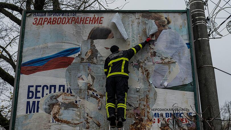 Ein ukrainischer Feuerwehrmann reißt in der kürzlich befreiten Stadt Cherson ein russisches Werbeplakat von einer Werbetafel.