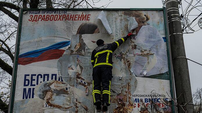 Ein ukrainischer Feuerwehrmann reißt in der kürzlich befreiten Stadt Cherson ein russisches Werbeplakat von einer Werbetafel.