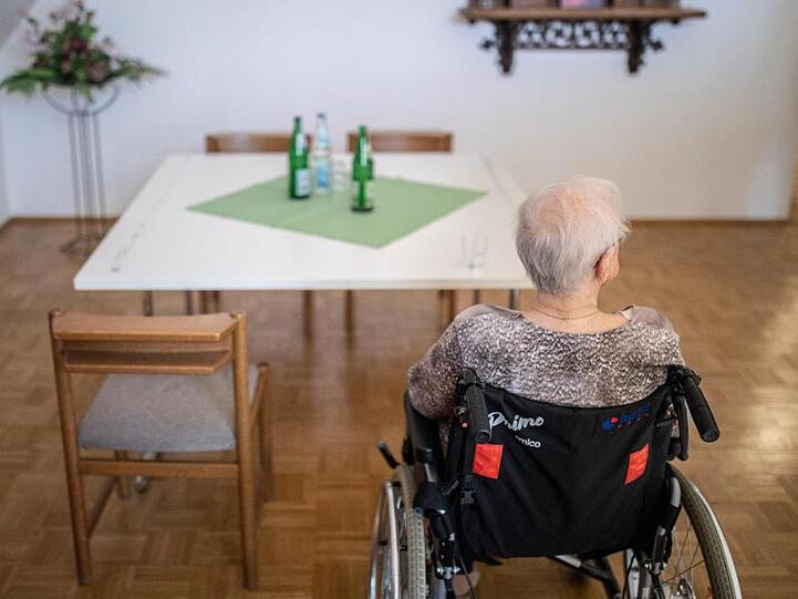 Eine ältere Frau sitzt in einem Pflegeheim in ihrem Rollstuhl vor einem Tisch. Foto: Marcel Kusch/dpa/Symbolbild