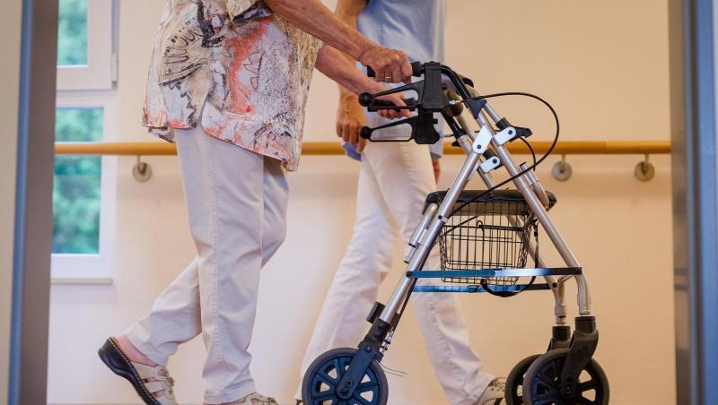 Eine Pflegekraft geht in einem Pflegeheim mit einer älteren Dame über einen Korridor.