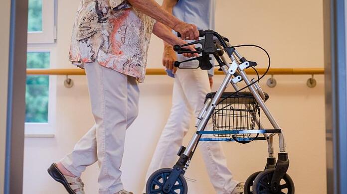 Eine Pflegekraft geht in einem Pflegeheim mit einer älteren Dame über einen Korridor.