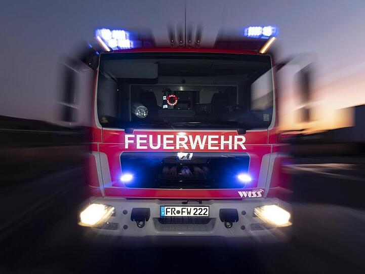 Ein Feuerwehrfahrzeug steht mit eingeschaltetem Blaulicht im Sonnenuntergang auf einer Straße. Foto: Patrick Seeger/dpa